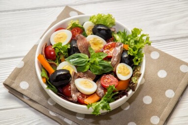 Close up. French cuisine. Traditional niçoise (nicoise) salad in a white plate on a polka dot napkin. White background.