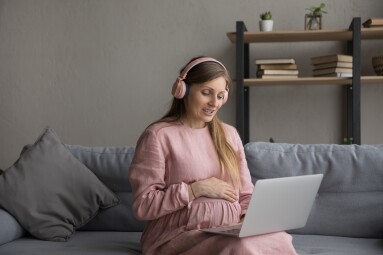 Happy,Young,Pregnant,Woman,In,Headphones,Looking,At,Computer,Screen,