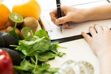 Nutritionist,Woman,Writing,Diet,Plan,On,Table,Full,Of,Fruits
