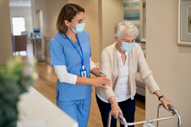 Smiling,Nurse,With,Face,Mask,Helping,Senior,Woman,To,Walk