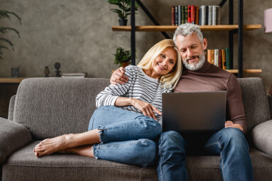 Senior,Couple,Using,Laptop,And,Smiling,While,Resting,On,Couch