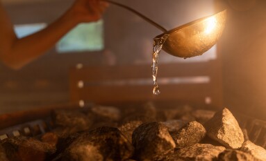 Woman,Pouring,Water,Onto,Hot,Stone,In,Sauna,Room,With