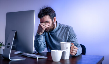 tired-man-sits-front-computer-with-cup-coffee-colored-lighting