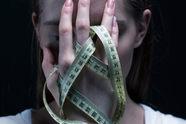 Anorexic,Girl,Covering,Her,Face,With,A,Centimeter