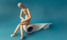Wooden,Figure,Sit,On,A,Roll,Of,Toilet,Paper.,Concept