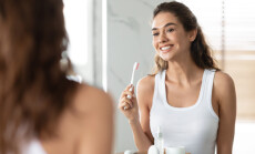 Woman,Brushing,Teeth,Holding,Toothbrush,Smiling,To,Mirror,In,Bathroom