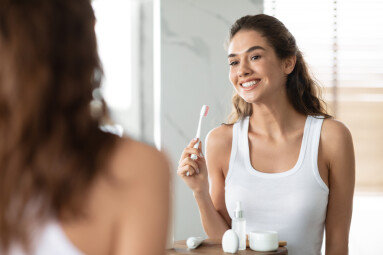 Woman,Brushing,Teeth,Holding,Toothbrush,Smiling,To,Mirror,In,Bathroom