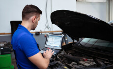 Young confident handsome car mechanic with laptop in hand conduc