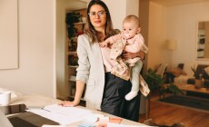 Creative,Businesswoman,Holding,Her,Baby,While,Standing,Behind,Her,Desk.