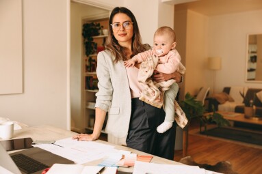 Creative,Businesswoman,Holding,Her,Baby,While,Standing,Behind,Her,Desk.