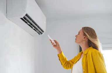 Woman,Holding,Remote,Control,Aimed,At,The,Air,Conditioner.