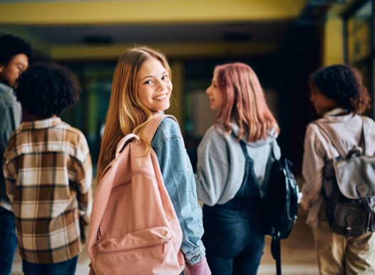 Happy,Teenage,Girl,Walking,Through,High,School,Hallway,With,Her