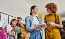 Happy,Teenage,Boy,And,Girl,Holding,Gadgets,Near,Classmates,In