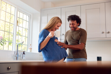 Couple,With,Pregnant,Wife,In,Kitchen,With,Husband,Touching,His