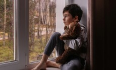 A,Sad,Boy,Looks,Out,The,Window,,Hugging,A,Teddy