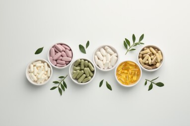 Different,Vitamin,Capsules,In,Bowls,And,Leaves,On,White,Background,