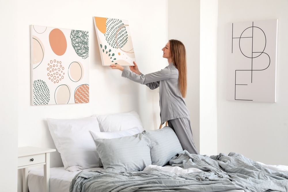 Young,Woman,Hanging,Painting,On,Light,Wall,In,Bedroom