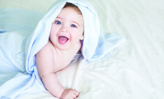 Newborn toddler boy laughing on the bed and looking at the camera