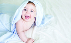 Newborn toddler boy laughing on the bed and looking at the camera