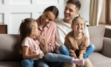 Happy,Young,Mother,And,Father,With,Two,Little,Daughters,Sitting
