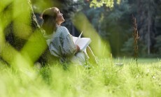 A,Young,Woman,Sits,In,A,Park,Leaning,Against,A