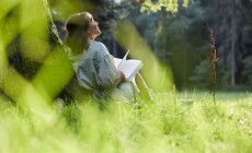 A,Young,Woman,Sits,In,A,Park,Leaning,Against,A