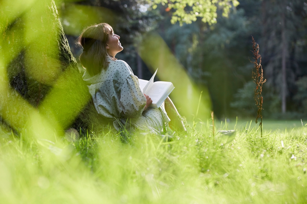 A,Young,Woman,Sits,In,A,Park,Leaning,Against,A