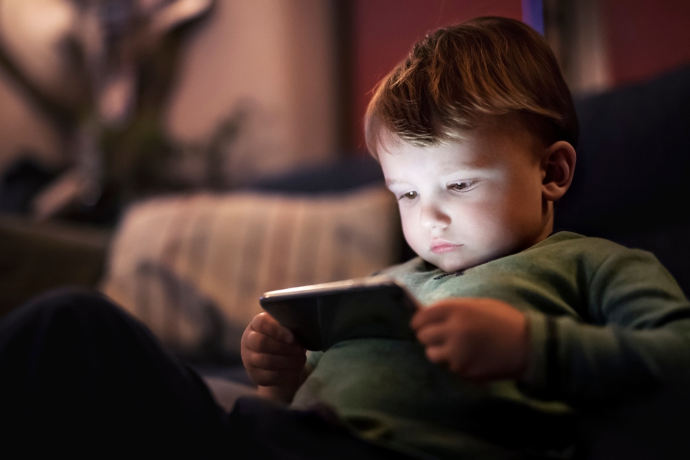Cute,Boy,Sitting,On,Bed,Watching,Something,On,Smartphone.,Children's