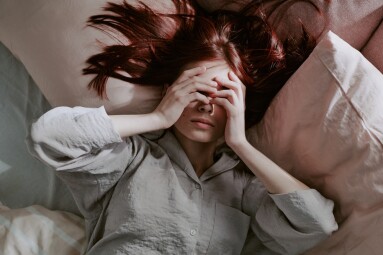 Woman,Lying,On,Bed,Covering,Her,Face,With,Hands,,Her