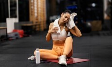 Exhausted,Sportswoman,Sitting,On,A,Gym,Floor,And,Wiping,Sweat