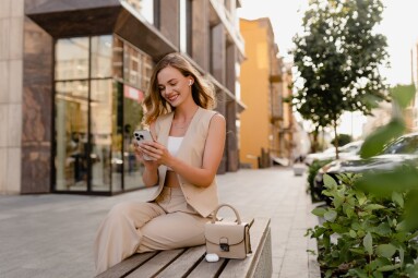 Attractive,Young,Blond,Woman,Sitting,In,City,Street,Using,Smart