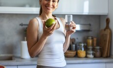A,Smiling,Young,Woman,Holds,An,Apple,And,A,Glass