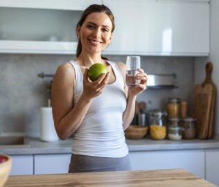 A,Smiling,Young,Woman,Holds,An,Apple,And,A,Glass