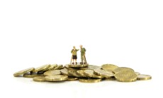 Elderly,Couple,Miniatures,Stand,Atop,A,Pile,Of,Gold,Coins,
