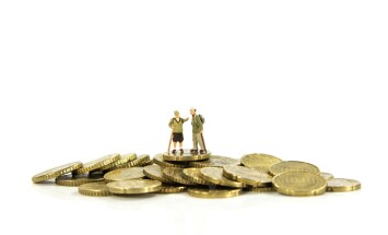 Elderly,Couple,Miniatures,Stand,Atop,A,Pile,Of,Gold,Coins,