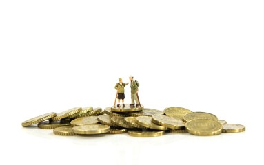 Elderly,Couple,Miniatures,Stand,Atop,A,Pile,Of,Gold,Coins,
