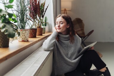 Young,Woman,Relaxed,At,Heater,With,Tablet,In,Hand