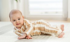 Smiling,Infant,In,Striped,Pajamas,Lying,On,Side,,Learning,To