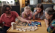 Family,Sitting,At,Table,Playing,Board,Game,,With,Three,Children