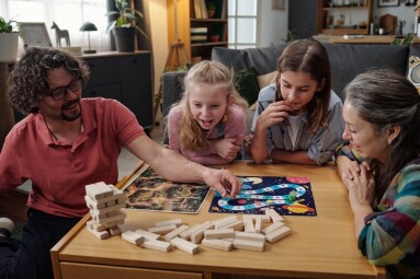 Family,Sitting,At,Table,Playing,Board,Game,,With,Three,Children
