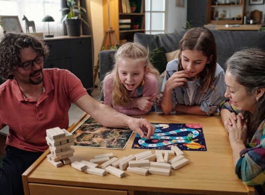 Family,Sitting,At,Table,Playing,Board,Game,,With,Three,Children