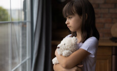 Close,Up,Lonely,Little,Girl,Hugging,Toy,,Looking,Out,Window,