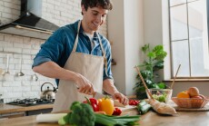 Young,Man,In,Apron,Standing,In,Home,Kitchen,Slicing,Vegetables