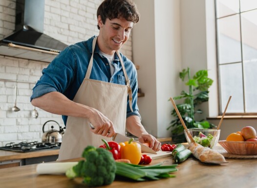 Young,Man,In,Apron,Standing,In,Home,Kitchen,Slicing,Vegetables